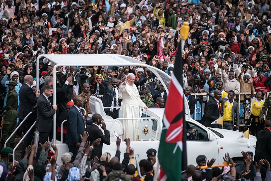 Man in an open pick-up waving to a crowd of people.