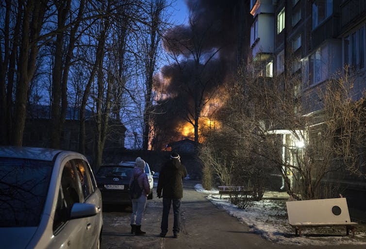 People stand on a street looking at a burning structure.