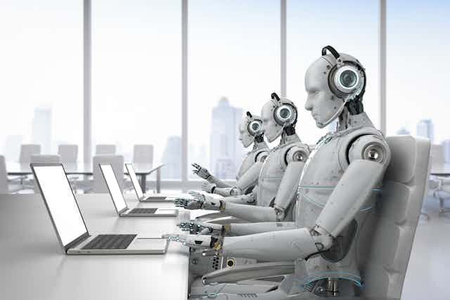 Tres robots trabajan en una oficina frente a unos ordenadores.