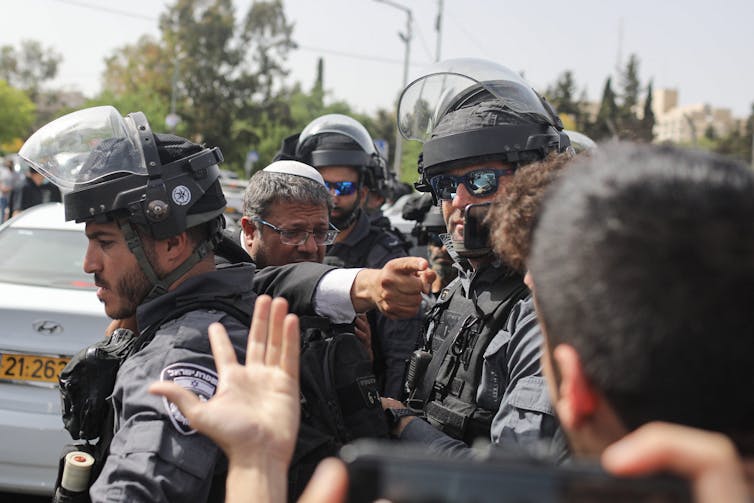 A man points toward another man as they are separated by police officers.