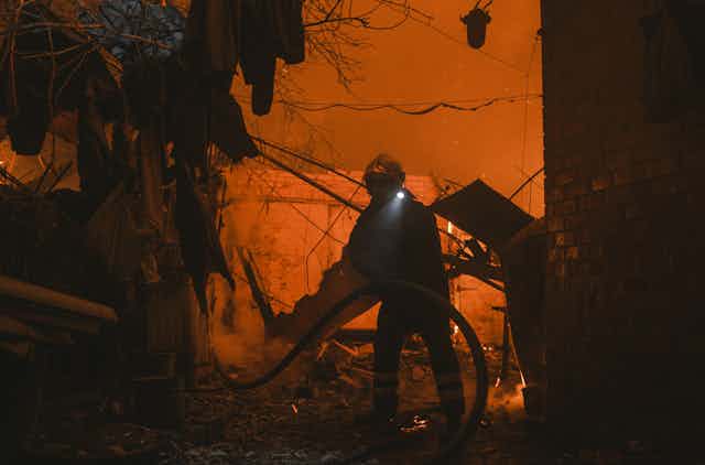 A firefighter tries to extinguish a blaze against a night sky lit up with fires.