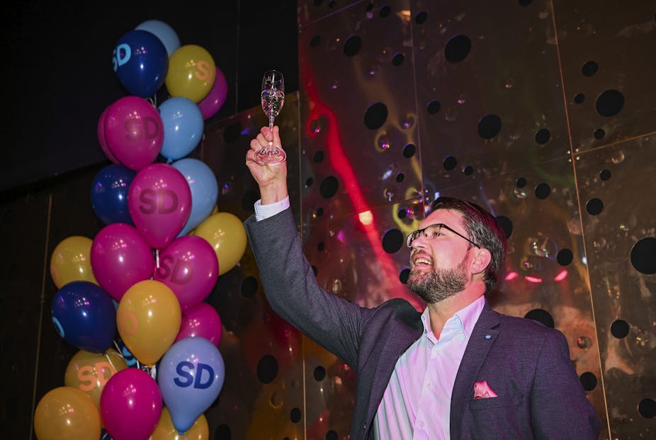 Jimmie Akesson lève une coupe de champagne sur fond de ballons multicolores marqués des lettres « SD », sigle de son parti
