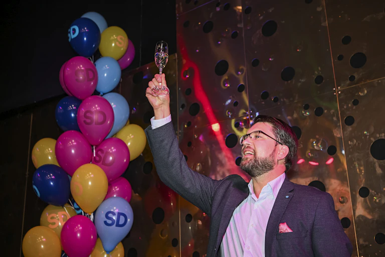 Jimmie Akesson lève une coupe de champagne sur fond de ballons multicolores marqués des lettres « SD », sigle de son parti