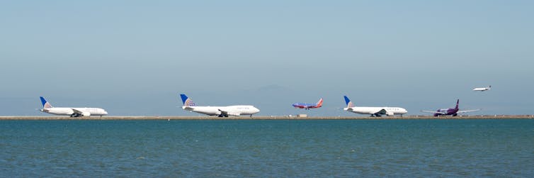 A number of planes line up for takeoff on a runway.