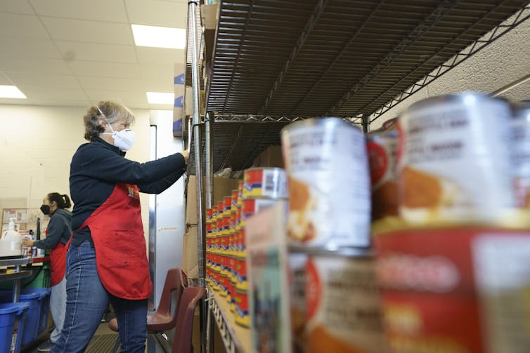 A woman in a red apron placing canned goods on shelves