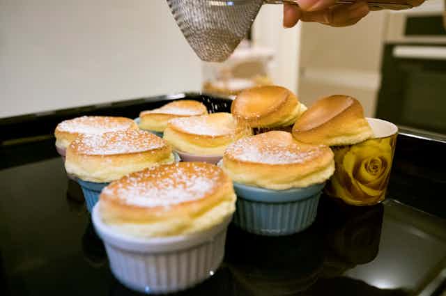 A tray of souffles with someone sprinkling sugar onto them.