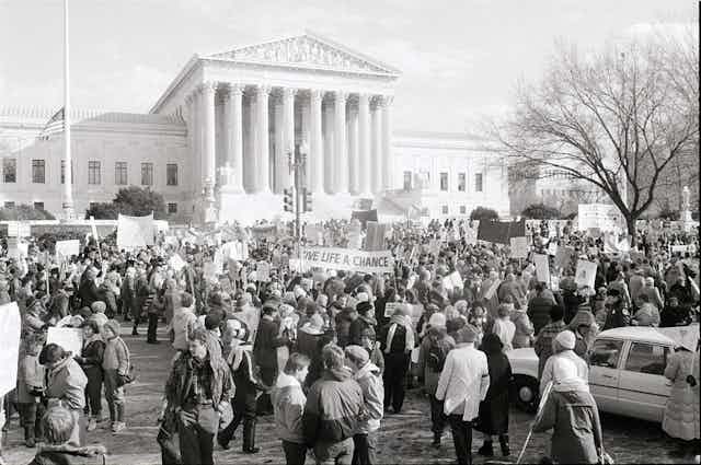 A black and white photo shows a crowd outside the US Supreme Court