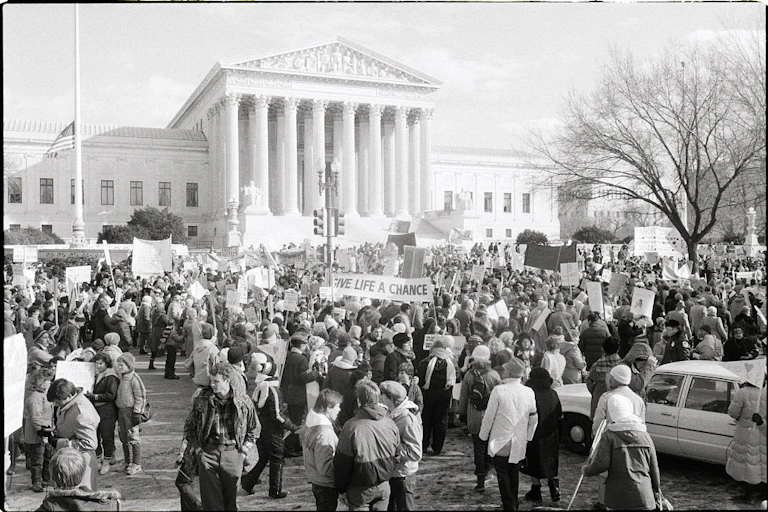 A black and white photo shows a crowd outside the US Supreme Court
