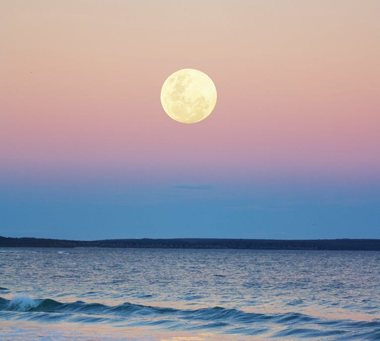 A photo of a full moon over the sea.