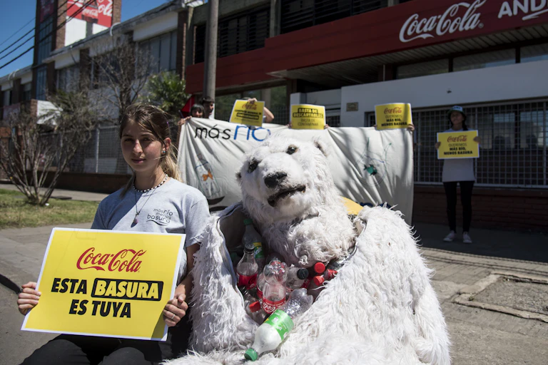 militante et ourse en peluche devant une usine coca cola