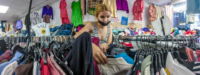 A blonde woman in a facemask rummages for second-hand clothes.