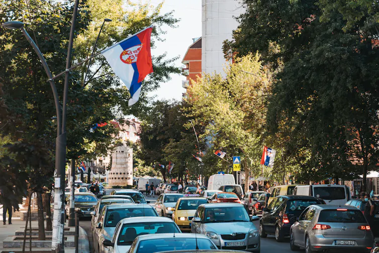 Serbian flags flying over a road crowded with cars.