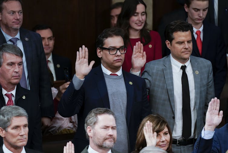 Two men in suits raise their hands, surrounded by other men and one women in formal clothing.