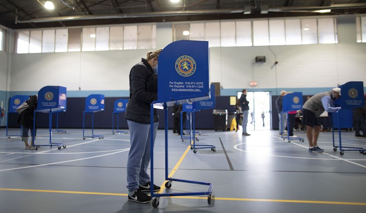 A person stands and leans into a voting box in a gymnasium.