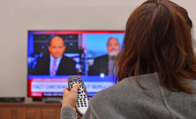 A person holding a remote watching the news on a TV.