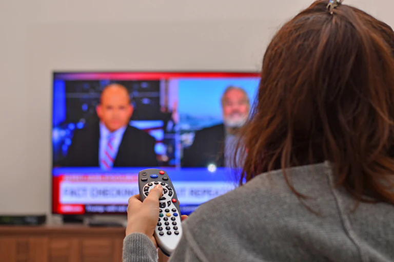 A person holding a remote watching the news on a TV.