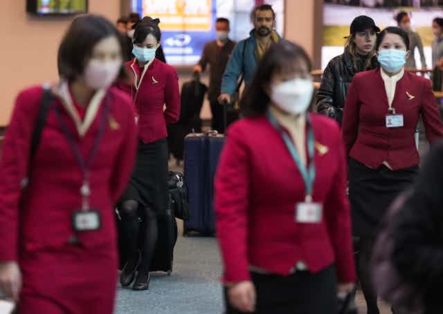 Women in red uniforms wearing face masks and badges on lanyards pulling travel bags