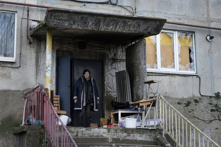 A resident who has remained in the city of Soledar is in front of the entrance to her building with windows destroyed by the explosions.
