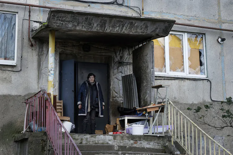 A resident who has remained in the city of Soledar is in front of the entrance to her building with windows destroyed by the explosions.