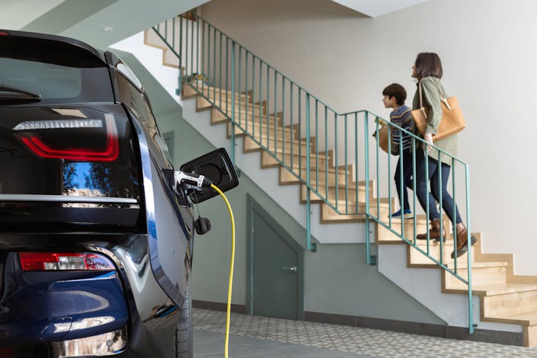 Mother and son head into house leaving electric vehicle plugged in to charger in the garage