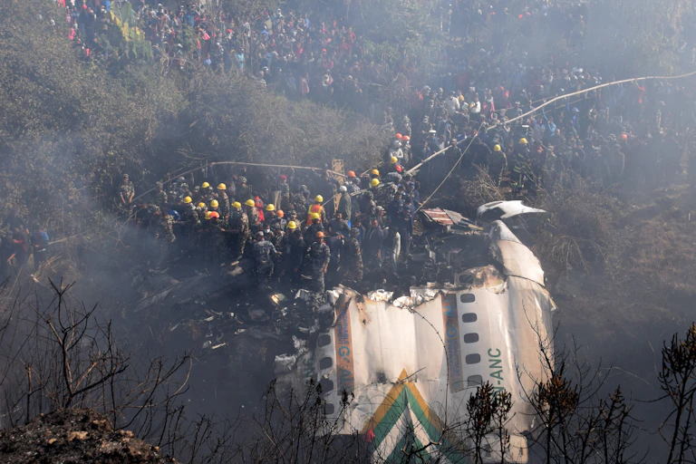 A long-distance view of a piece of an airplane and many people in yellow and orange hard hats descending down a slope to access it