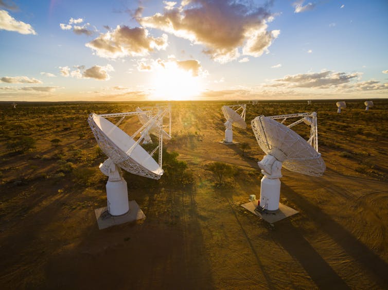 The ASKAP radio telescope, showing radio dishes pointed at a blue sky with the sun in the background.