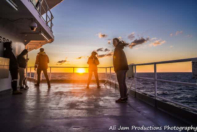 Four scientists stand on a vessel in the ocean at sunset