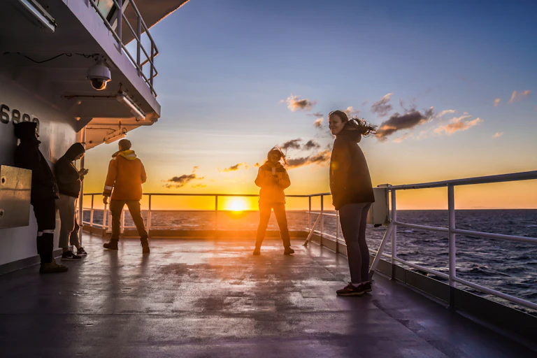 Four scientists stand on a vessel in the ocean at sunset