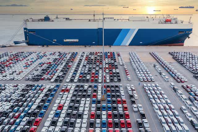Car carrier ship docked behind rows of cars