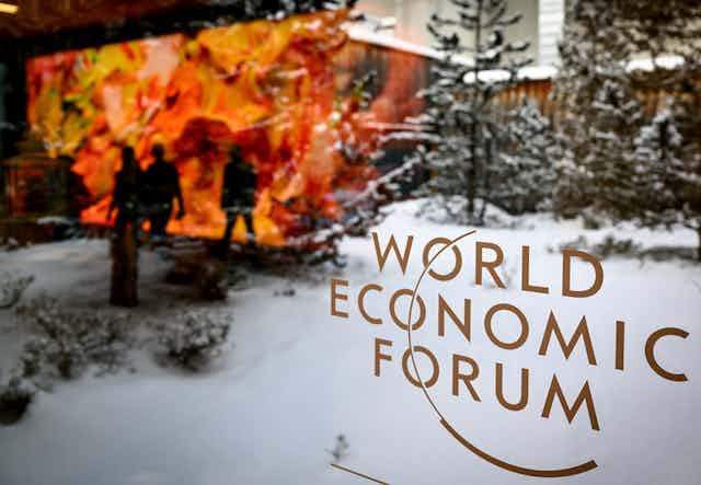 The logo of the WEF is pictured on a window of the Congress Center in front of snow covered trees as participants and artistic project 'Artificial Realities: Coral' from Turkish-American media artist Refik Anadol are reflected during the 52nd annual meeting of the World Economic Forum, WEF, in Davos, Switzerland, 16 January 2023.