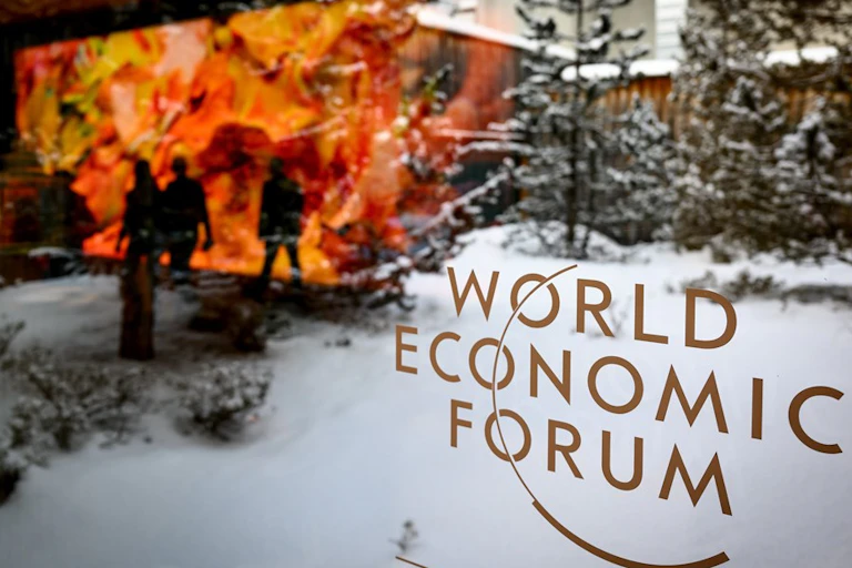 The logo of the WEF is pictured on a window of the Congress Center in front of snow covered trees as participants and artistic project 'Artificial Realities: Coral' from Turkish-American media artist Refik Anadol are reflected during the 52nd annual meeting of the World Economic Forum, WEF, in Davos, Switzerland, 16 January 2023.