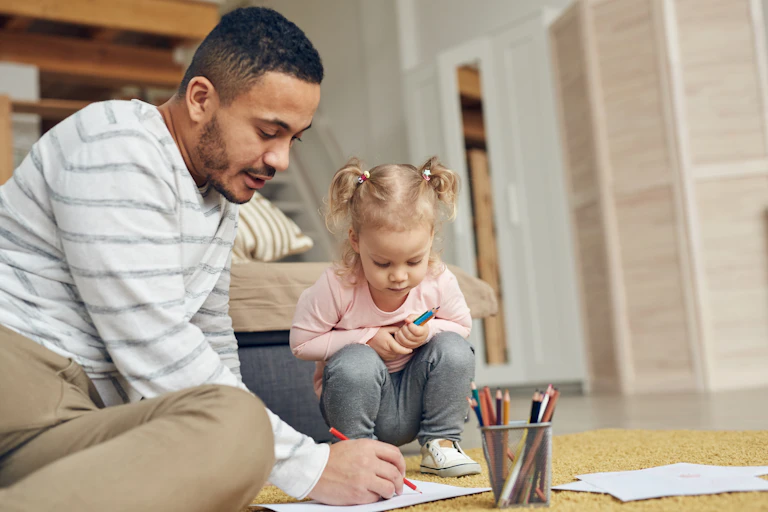 A father draws with his daughter on the floor.