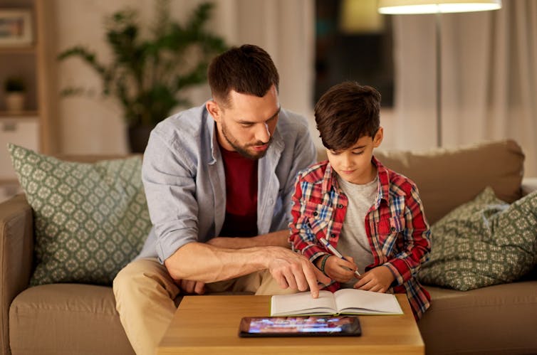 A father helps his son with reading.