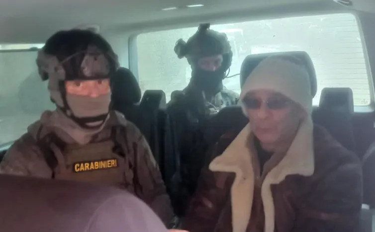 Matteo Messina Denaro in the back of a car with two heavily armoured police officers.