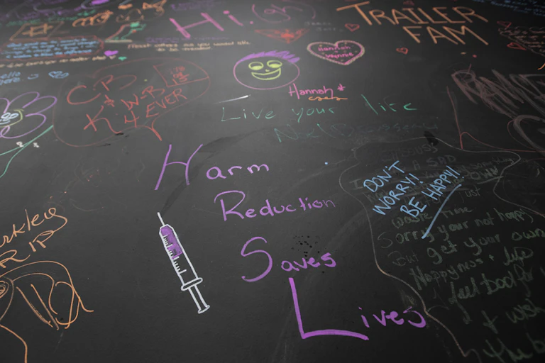 A wall with notes written in multi-coloured chalk. The one in the middle reads: Harm reduction saves lives.