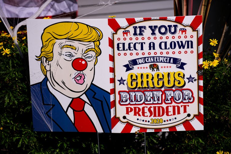A placard shows a cartoon Donald Trump with a red clown nose.