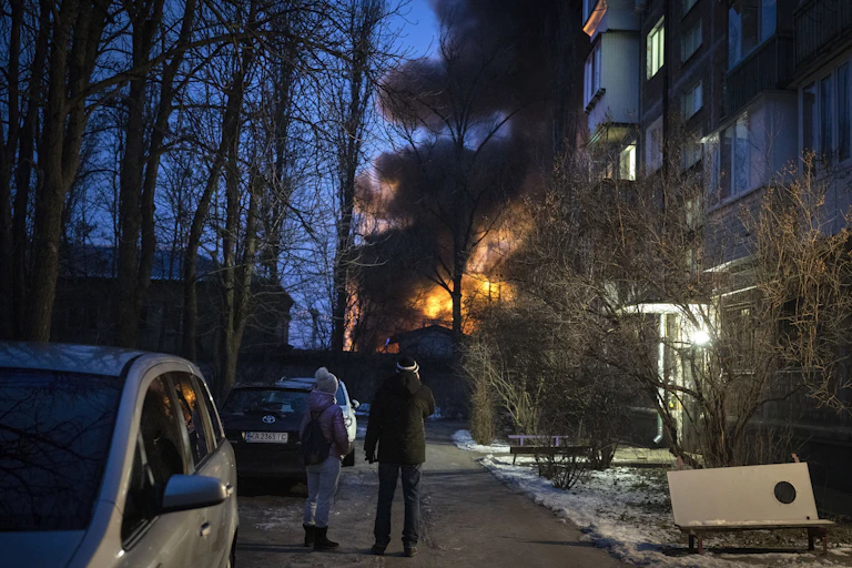 People stand on a street looking at a burning structure.
