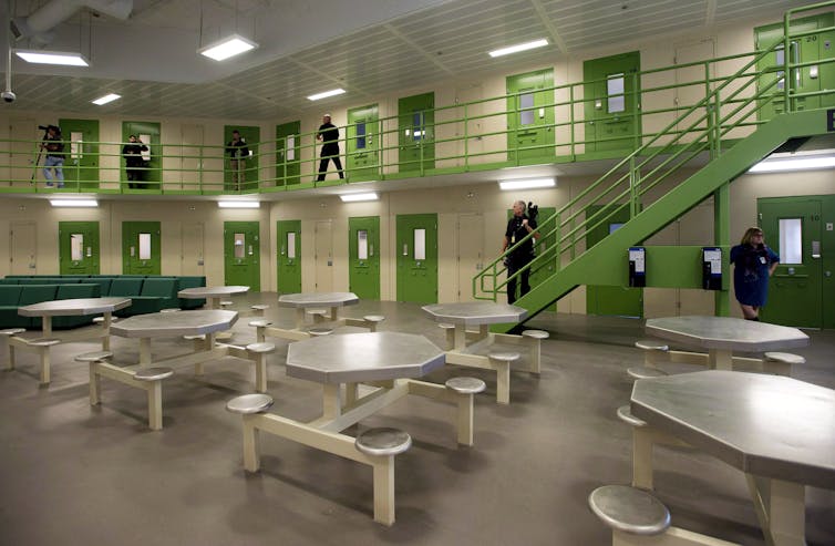 The inside of a detention centre, with metallic seating areas and green doors and staircases.