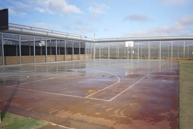 A fenced off outdoor area with a basketball court.