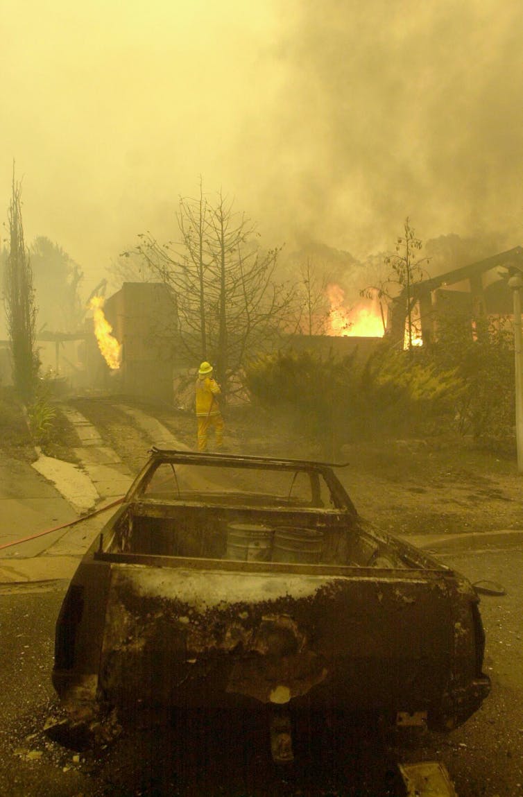 A burnt out car near a burning house