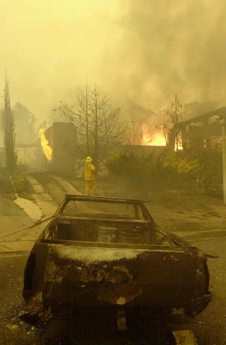 A burnt out car near a burning house