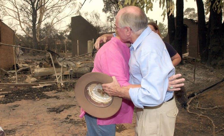 John Howard hugs a local near a burnt-out house