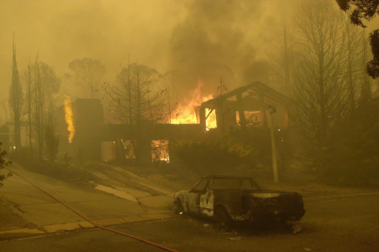 Burnt out car next to burning house