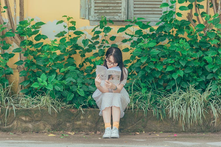 woman reading in front of greenery and house