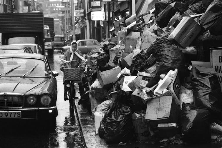 A woman cycles in a street full of rubbish.