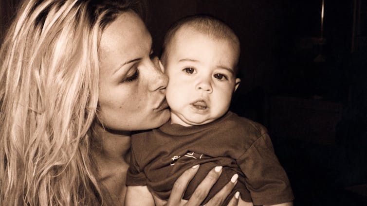 A sepia photograph shows Pamela Anderson kissing the cheek of her baby son. She has long blonde hair parted to the side.