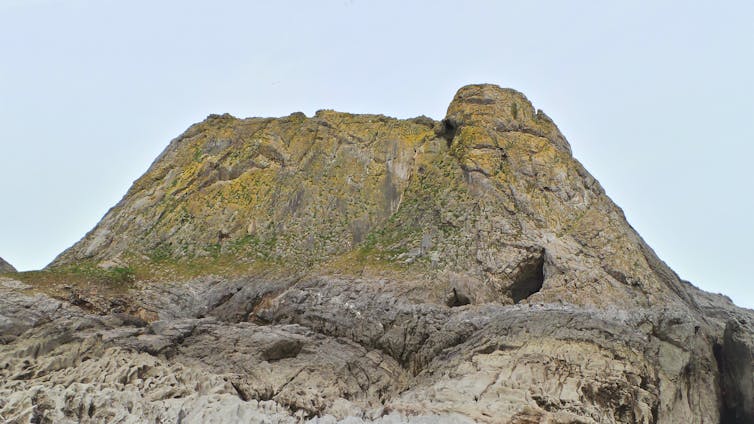 A large rocky mound with a small cave entrance.