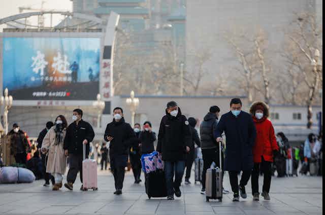 A group of masked people in Beijing walking with luggage.