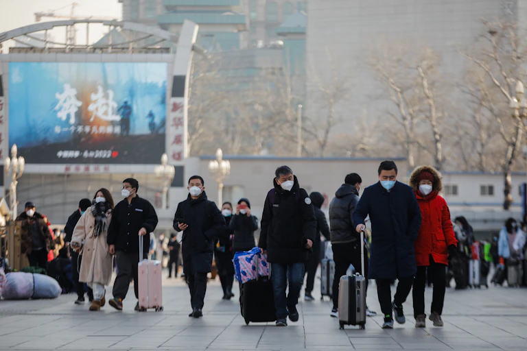 A group of masked people in Beijing walking with luggage.