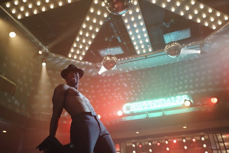 A topless black man wears a hat and trousers while performing for the Chippendales strip show.